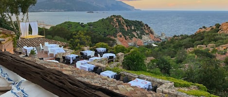 A coastal restaurant with outdoor seating overlooking the sea and hills.