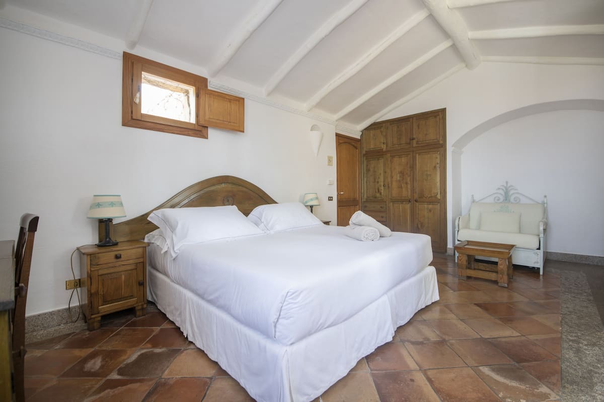 A bedroom with a large bed, wooden nightstands, a wooden wardrobe, and a white sofa.