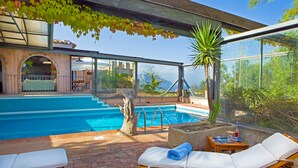 A poolside area with lounge chairs, a small table with a drink, and a view of the pool and surrounding landscape. - Hotel Monte Turri by Falkensteiner (Tortoli)