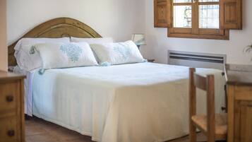 A neatly made bed with a wooden headboard, a bedside table, and a window with wooden shutters.
