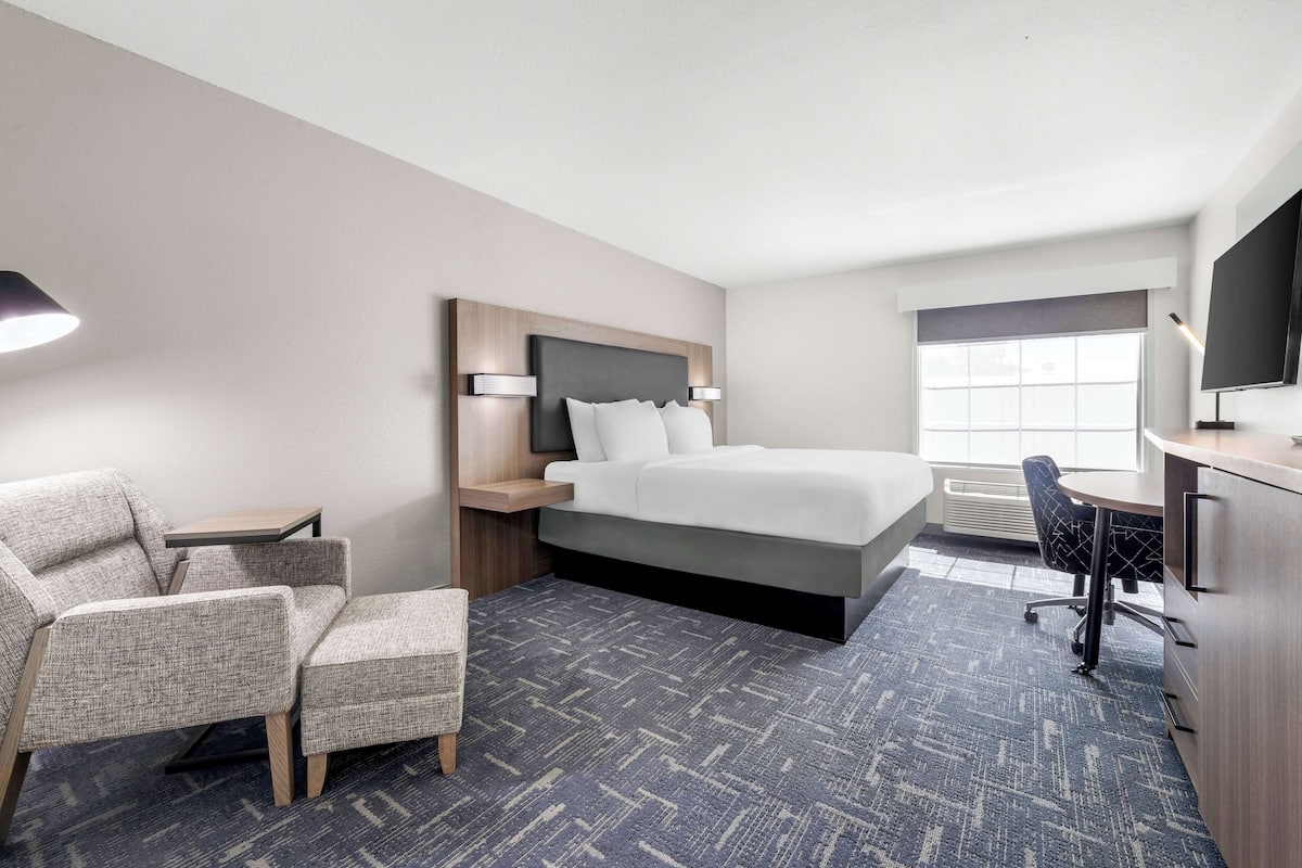 A hotel room with a bed, a desk, a chair, a TV, and a window.