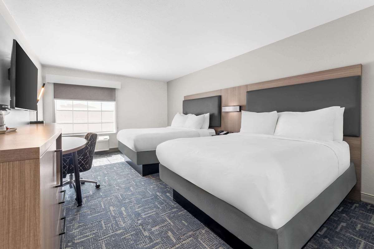 A hotel room with two beds, a desk, a chair, a TV, and a window with a view.