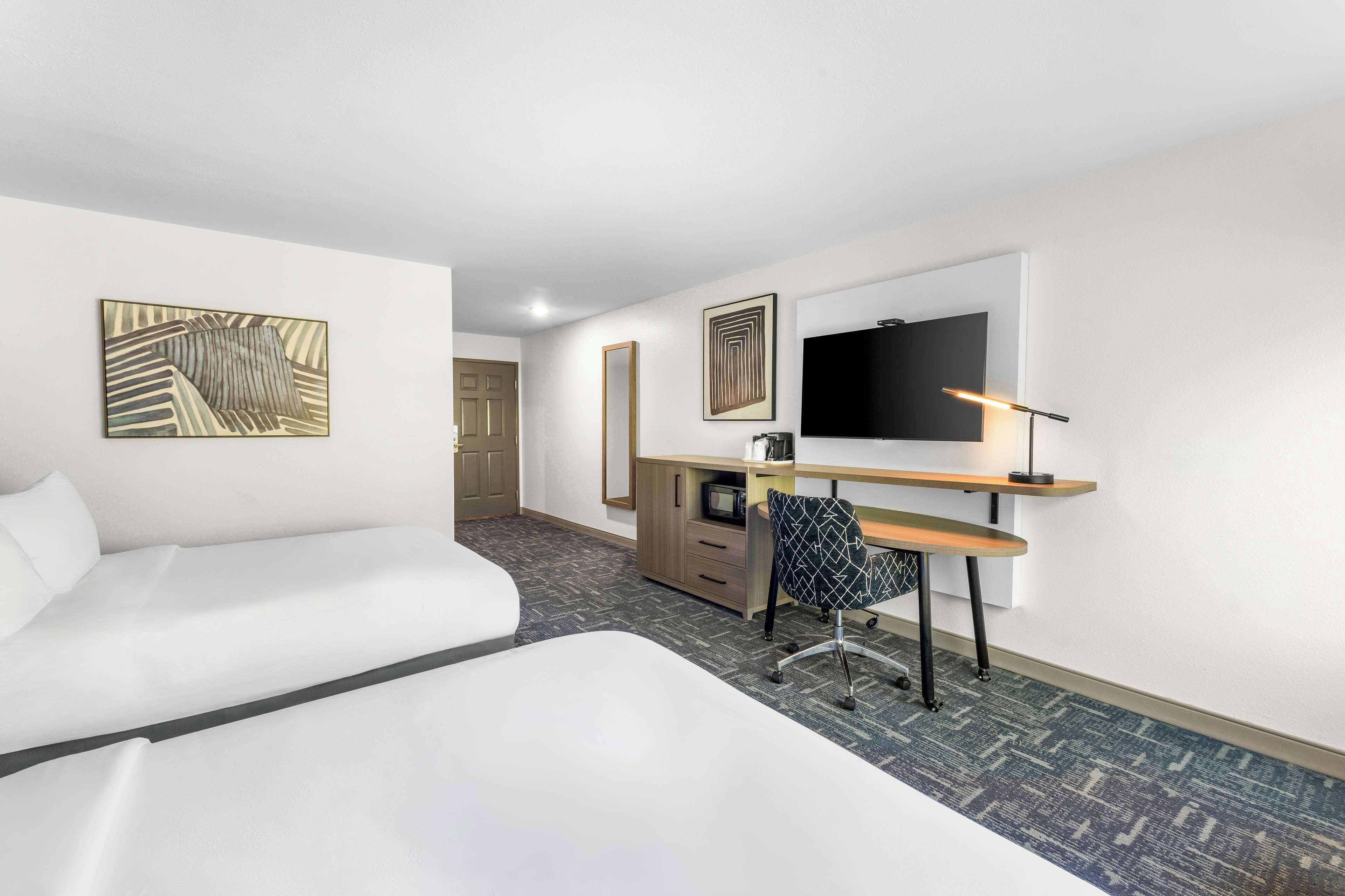 A hotel room with a bed, a desk with a chair, a television, and artwork on the walls.