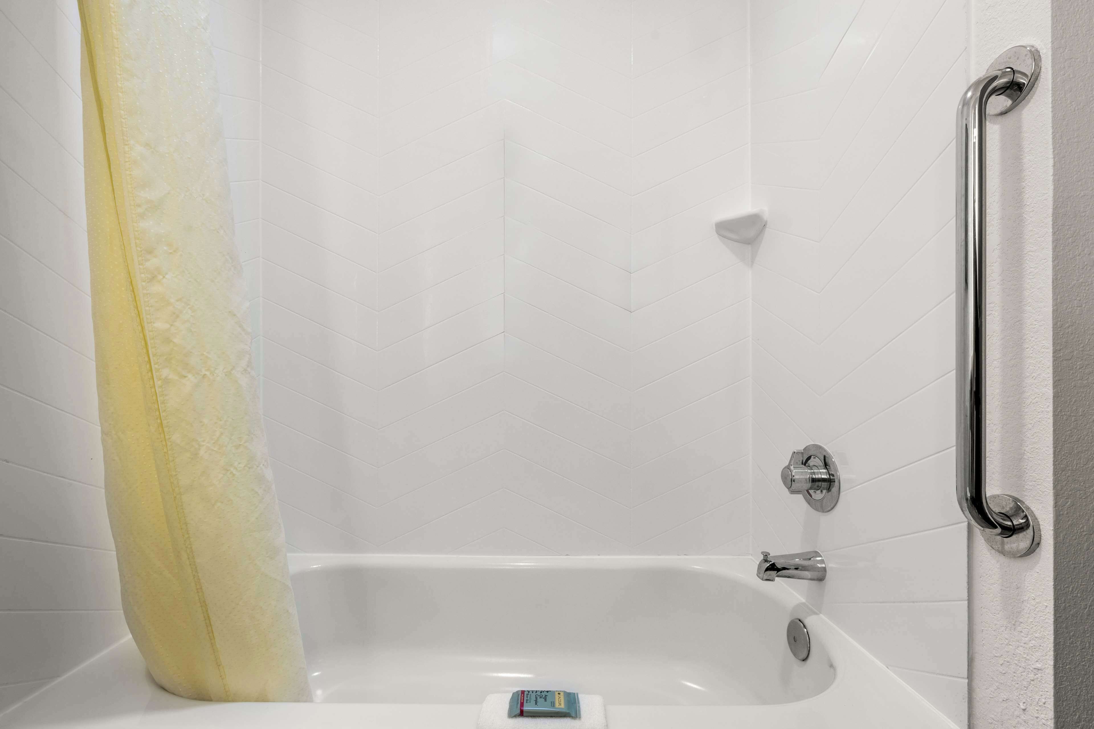 A white bathtub with a shower curtain, a grab bar on the right, and a soap dish on the tub.