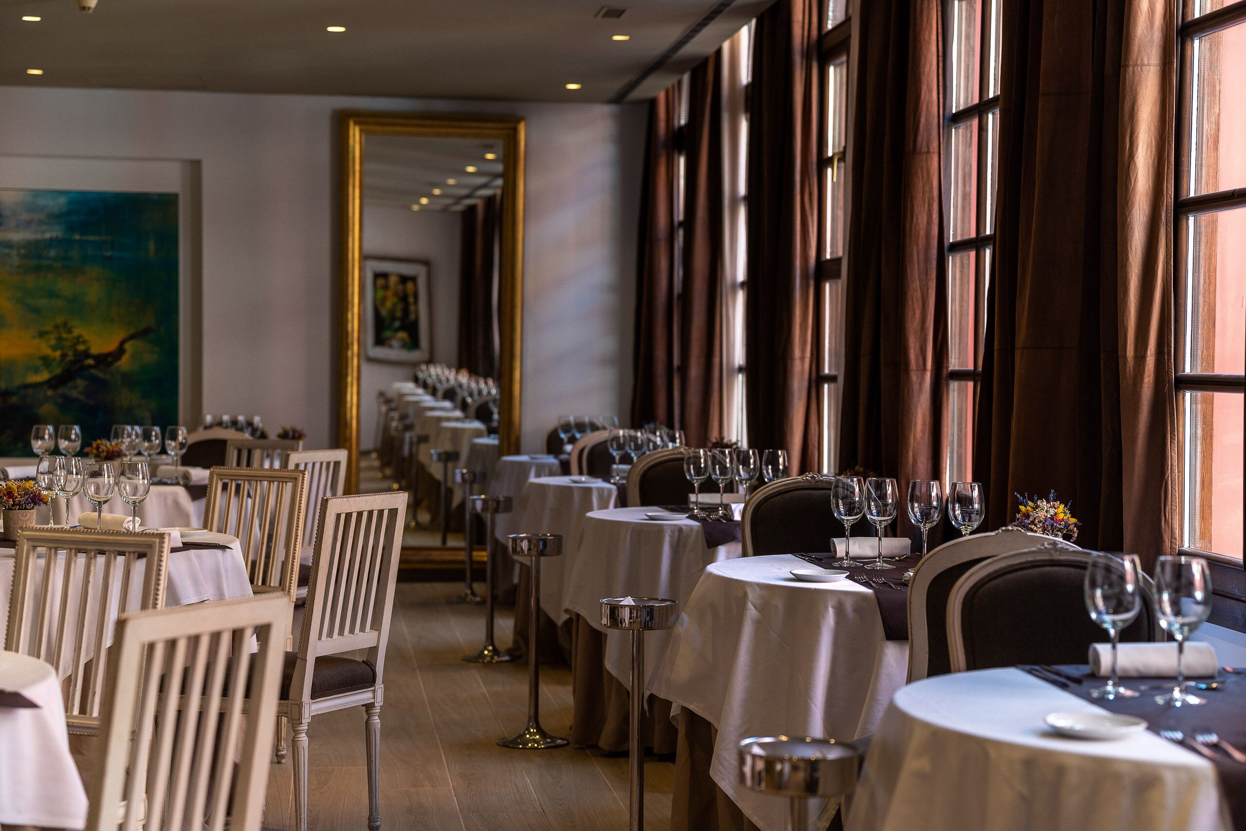 A restaurant with multiple tables and chairs, each set with wine glasses and cutlery.