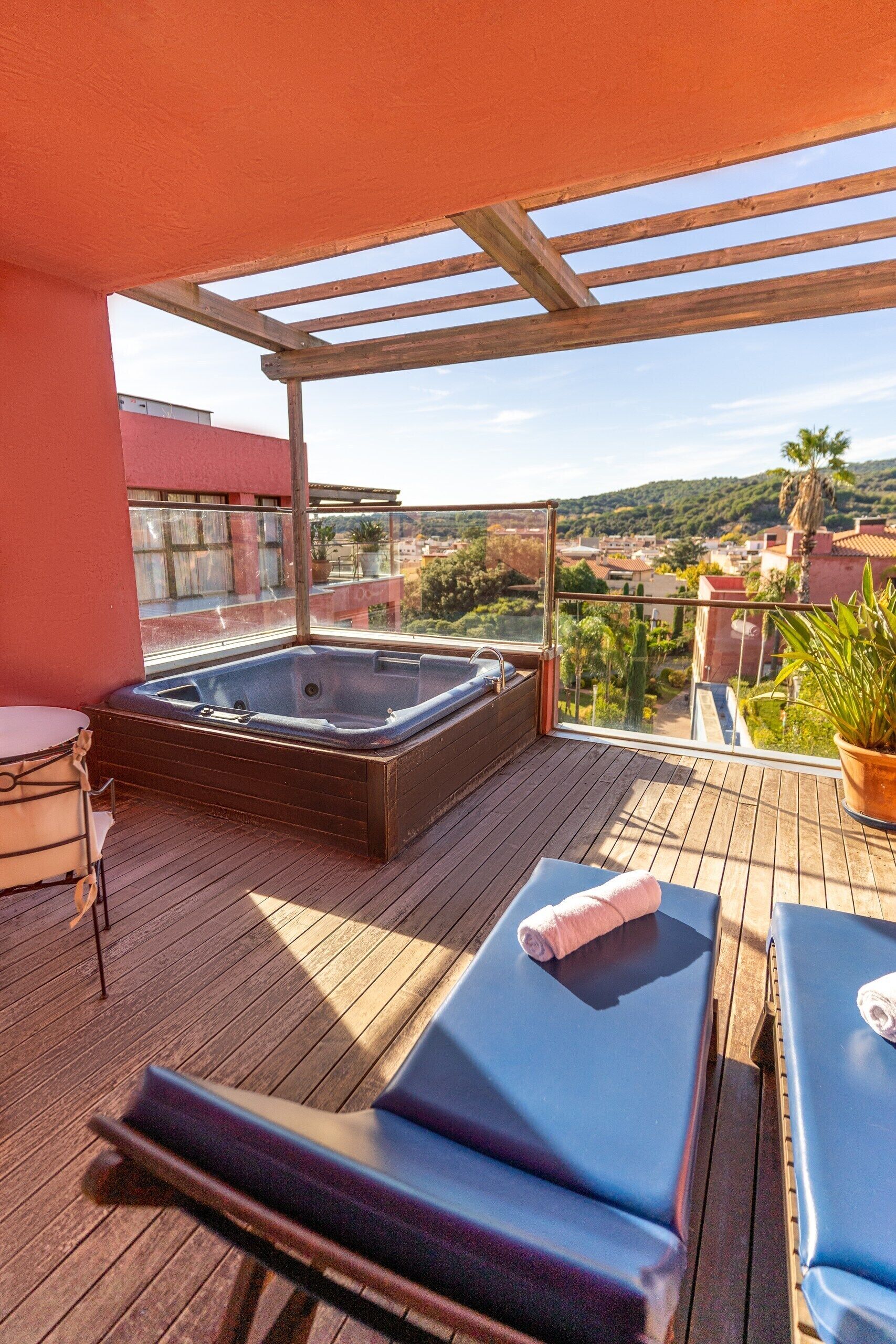 Una terraza de madera con un jacuzzi, sillas de descanso y vistas a un pueblo.