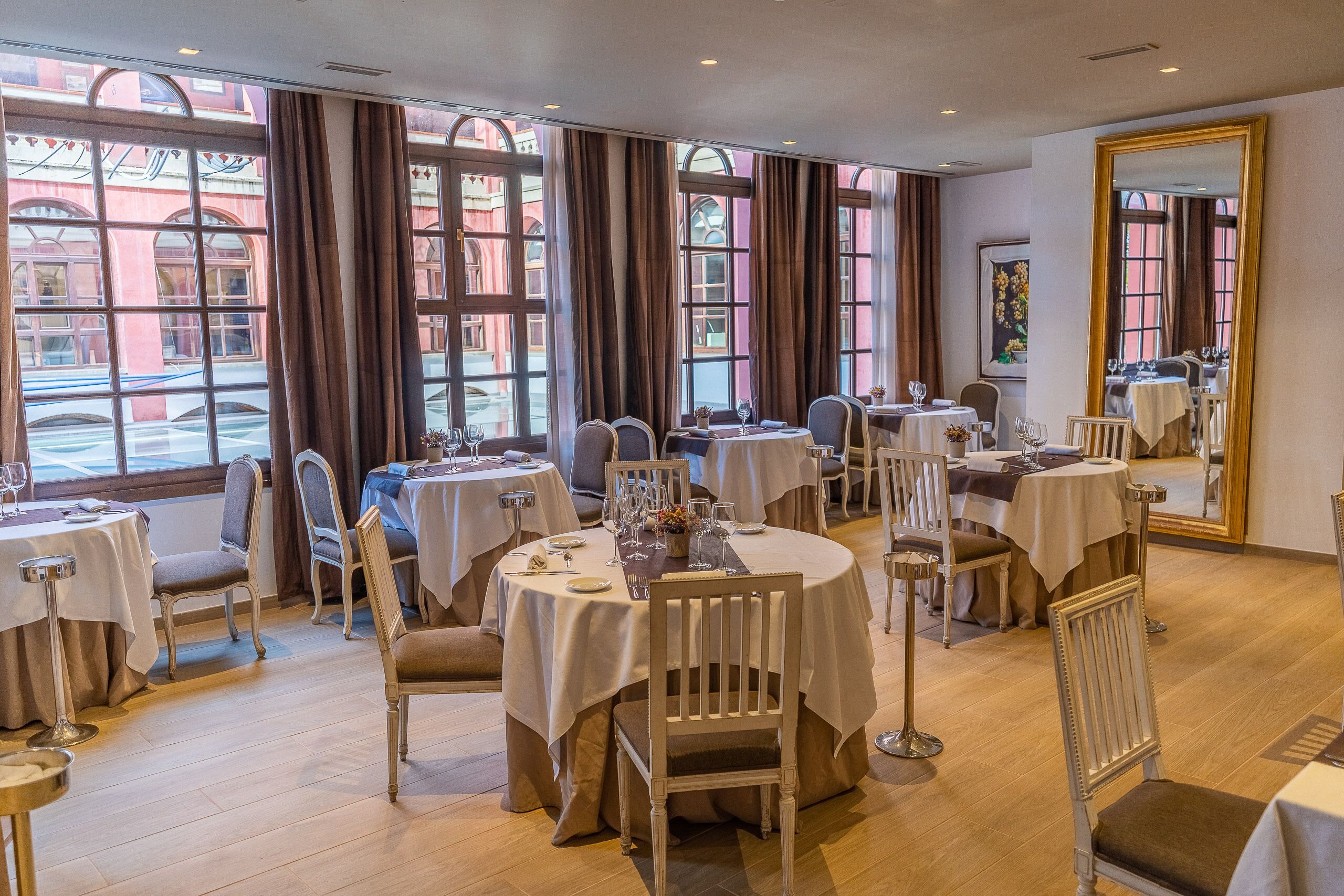 A restaurant with round tables, white tablecloths, and brown curtains.