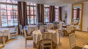 A restaurant with round tables, white tablecloths, and brown curtains.