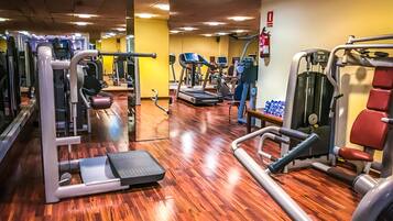 Un gimnasio con diversas máquinas de ejercicio, suelo de madera y pared amarilla.