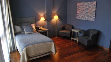 Una camera d'albergo con un letto, due poltrone, un comodino con una lampada e un quadro appeso al muro.