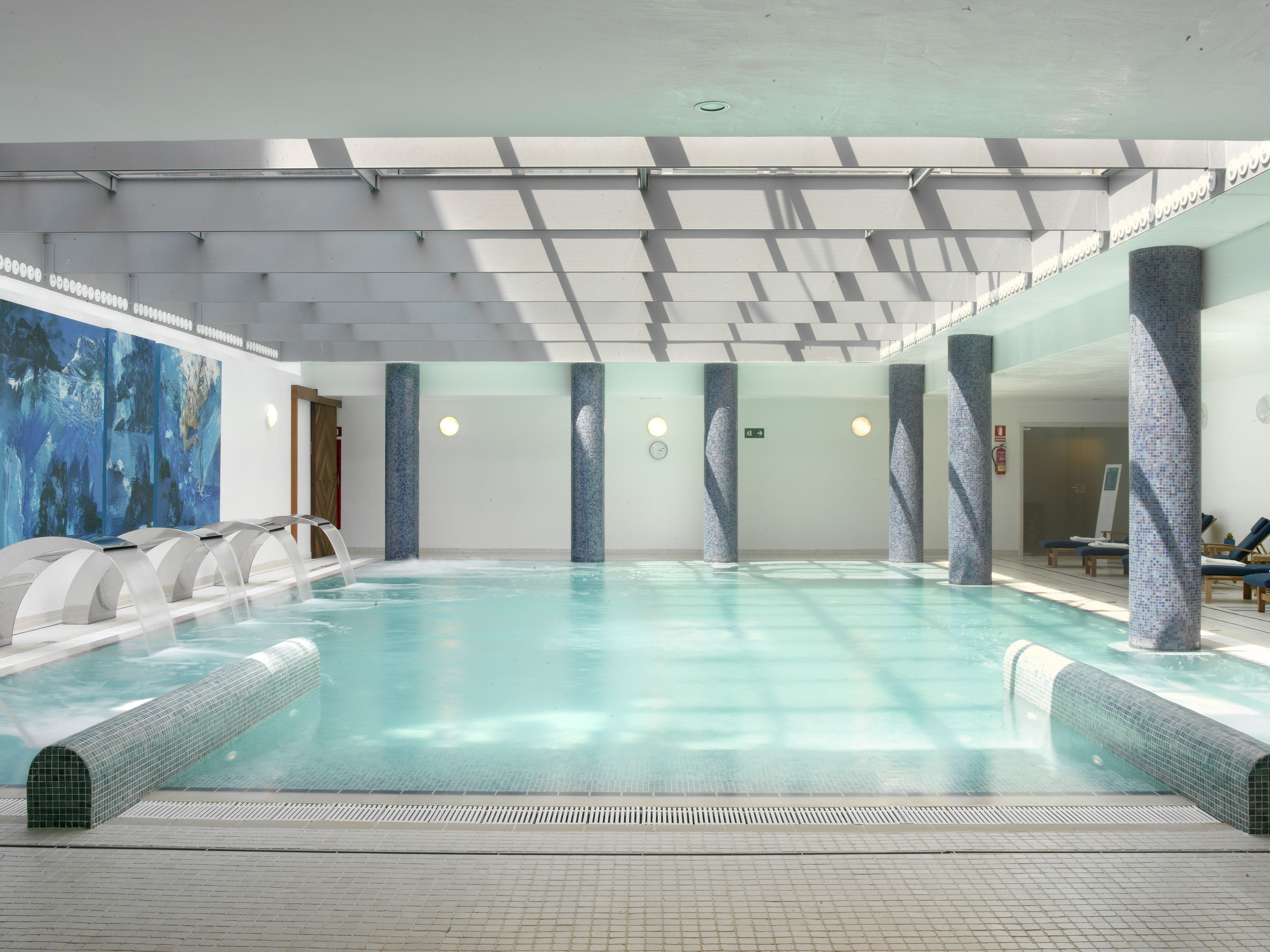 A large indoor swimming pool with clear water, surrounded by tiled walls and columns.