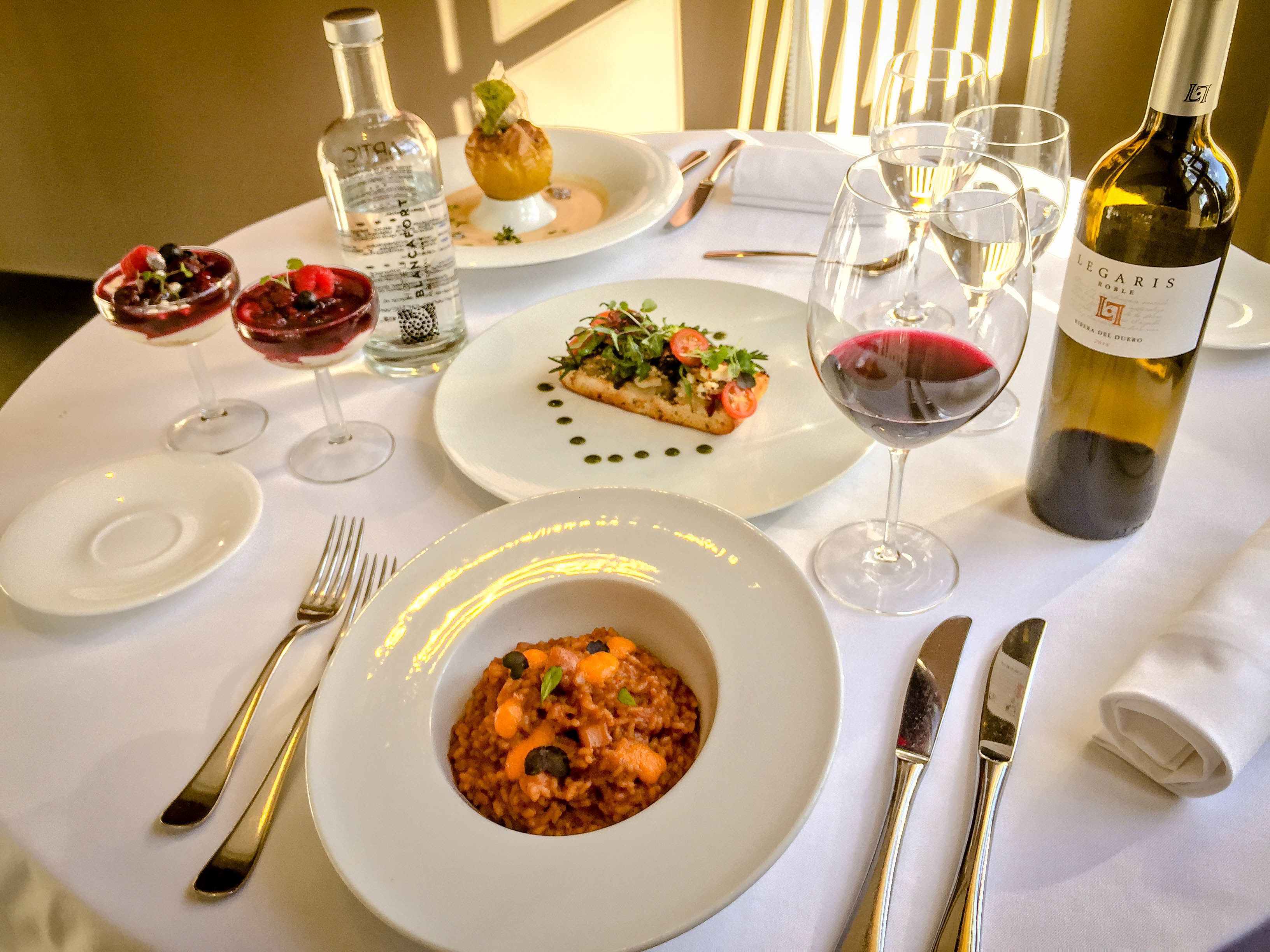 A table set for a meal with plates of food, glasses of wine, and cutlery.