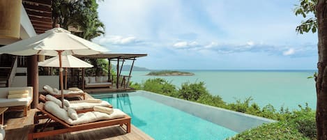 Una piscina infinita con sillones y sombrillas, con vistas al mar azul y una pequeña isla.