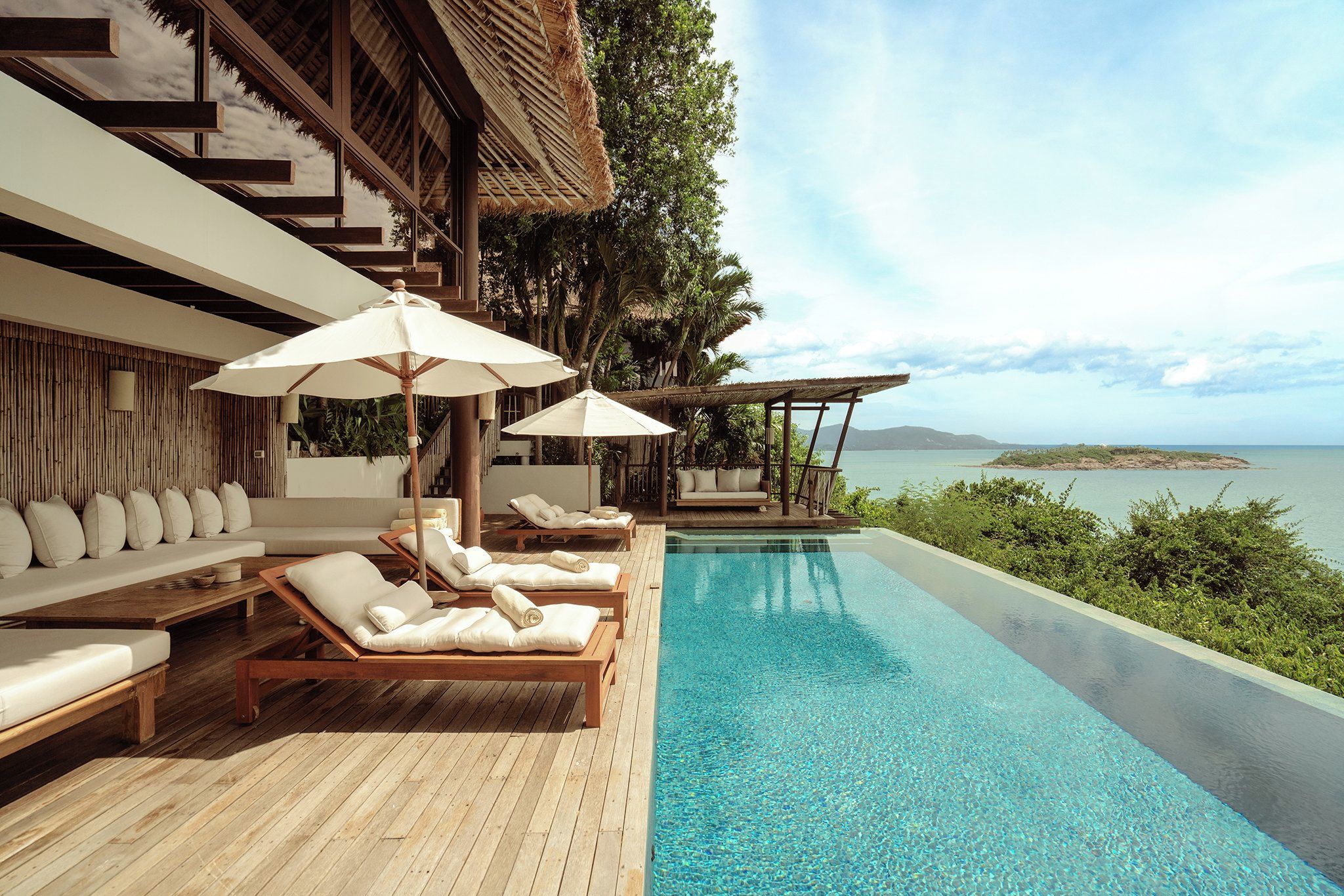 A poolside area with lounge chairs and umbrellas, overlooking a clear blue pool and a scenic view of the sea.