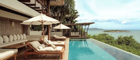 A poolside area with lounge chairs and umbrellas, overlooking a clear blue pool and a scenic view of the sea.