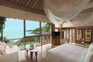 A spacious room with a large window offering a view of the sea, a comfortable sofa, a TV, and a wooden vanity with a mirror. - Six Senses Samui (Koh Samui)