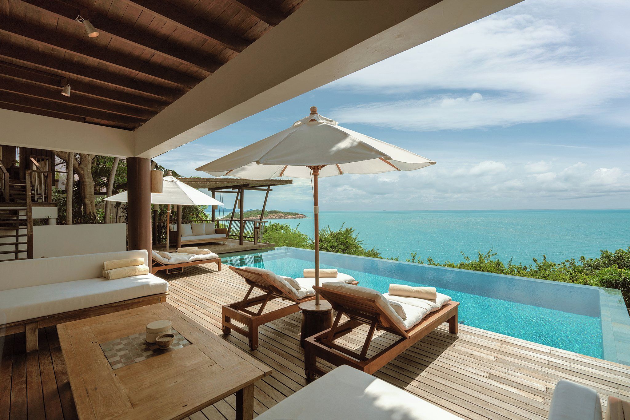 An infinity pool with a view of the ocean, wooden deck furniture, and umbrellas.