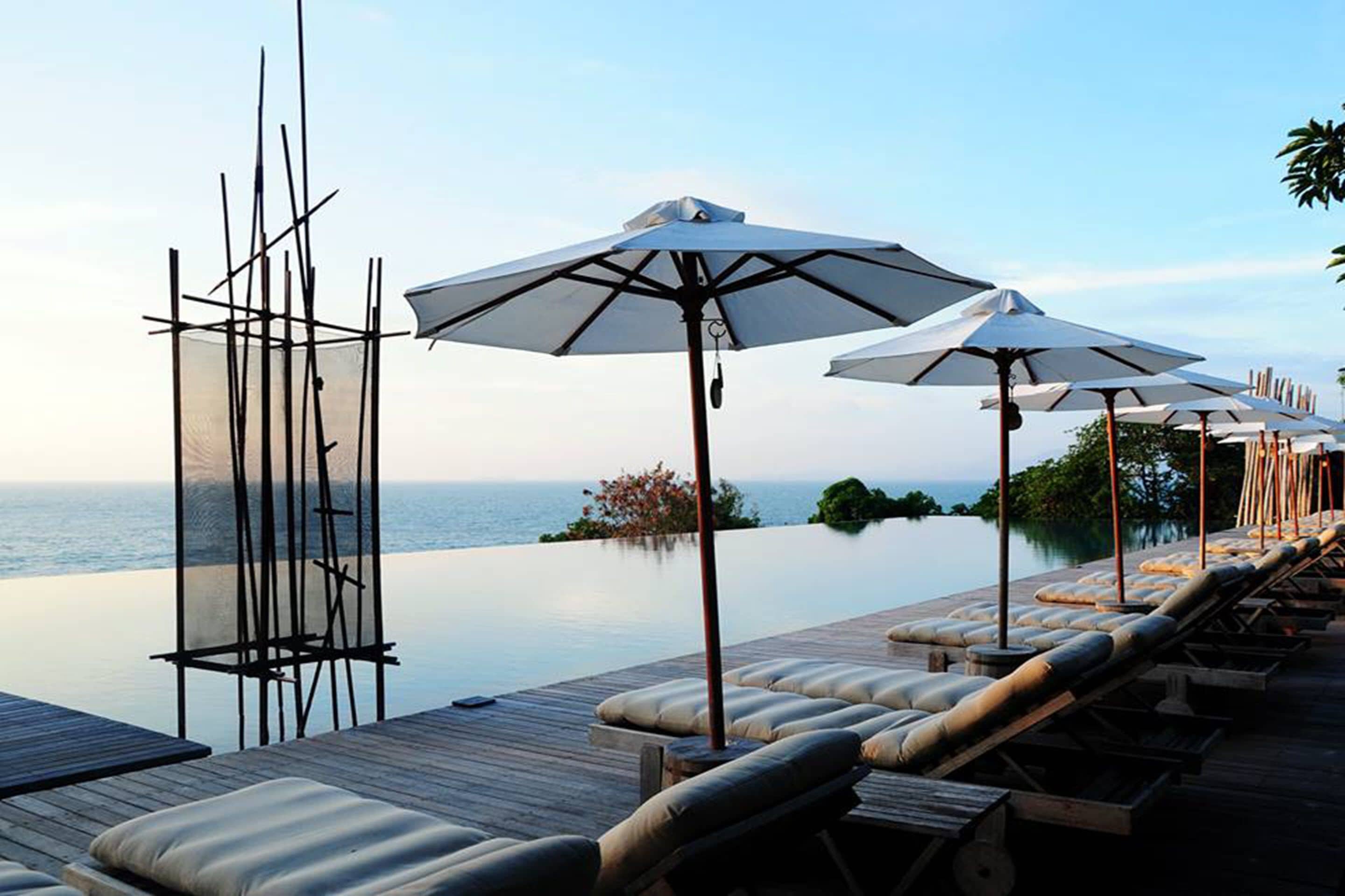 An infinity pool with lounge chairs and umbrellas, overlooking a calm sea.
