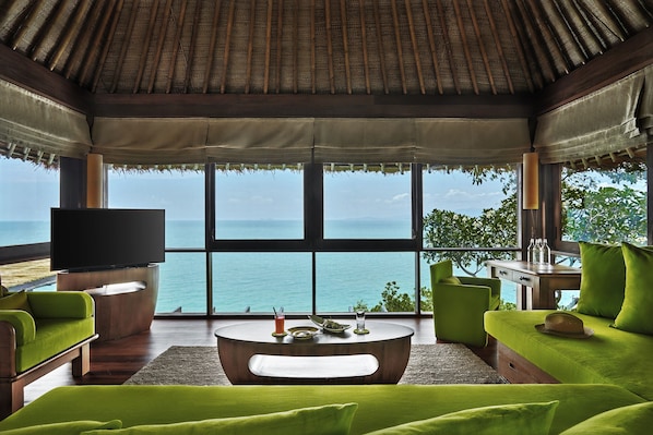 A modern living room with a large TV, green sofas, a coffee table, and a view of the ocean. - Six Senses Samui (Koh Samui)