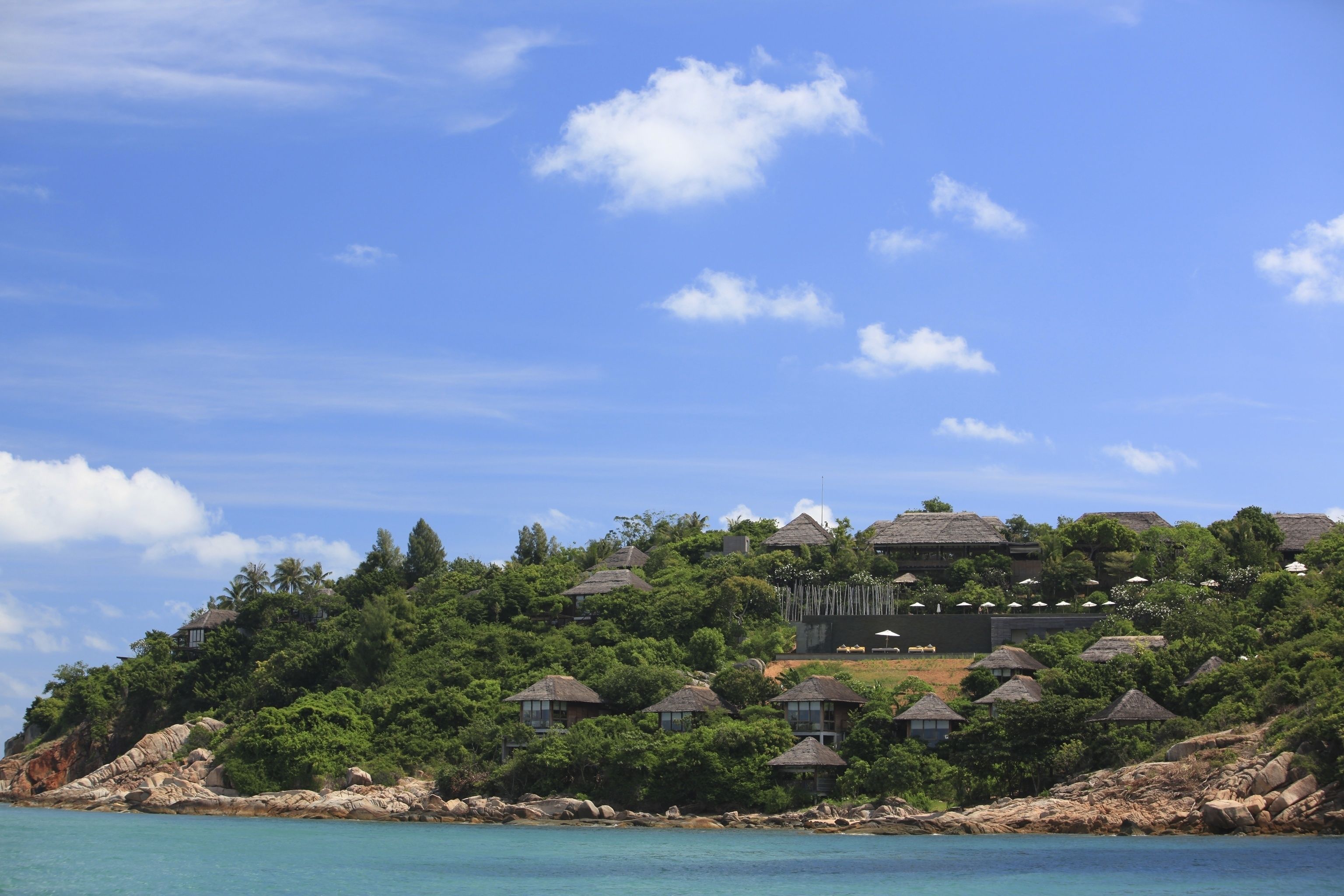 A coastal resort with thatched-roof cottages, lush greenery, and a clear blue sky.