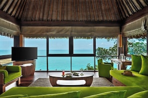 A room with a large window overlooking a body of water, a flat-screen TV, and green upholstered furniture. - Six Senses Samui (Koh Samui)