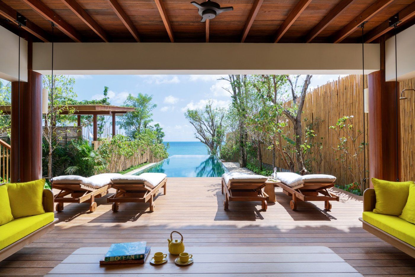 A wooden deck with lounge chairs and a table, overlooking a clear blue ocean.