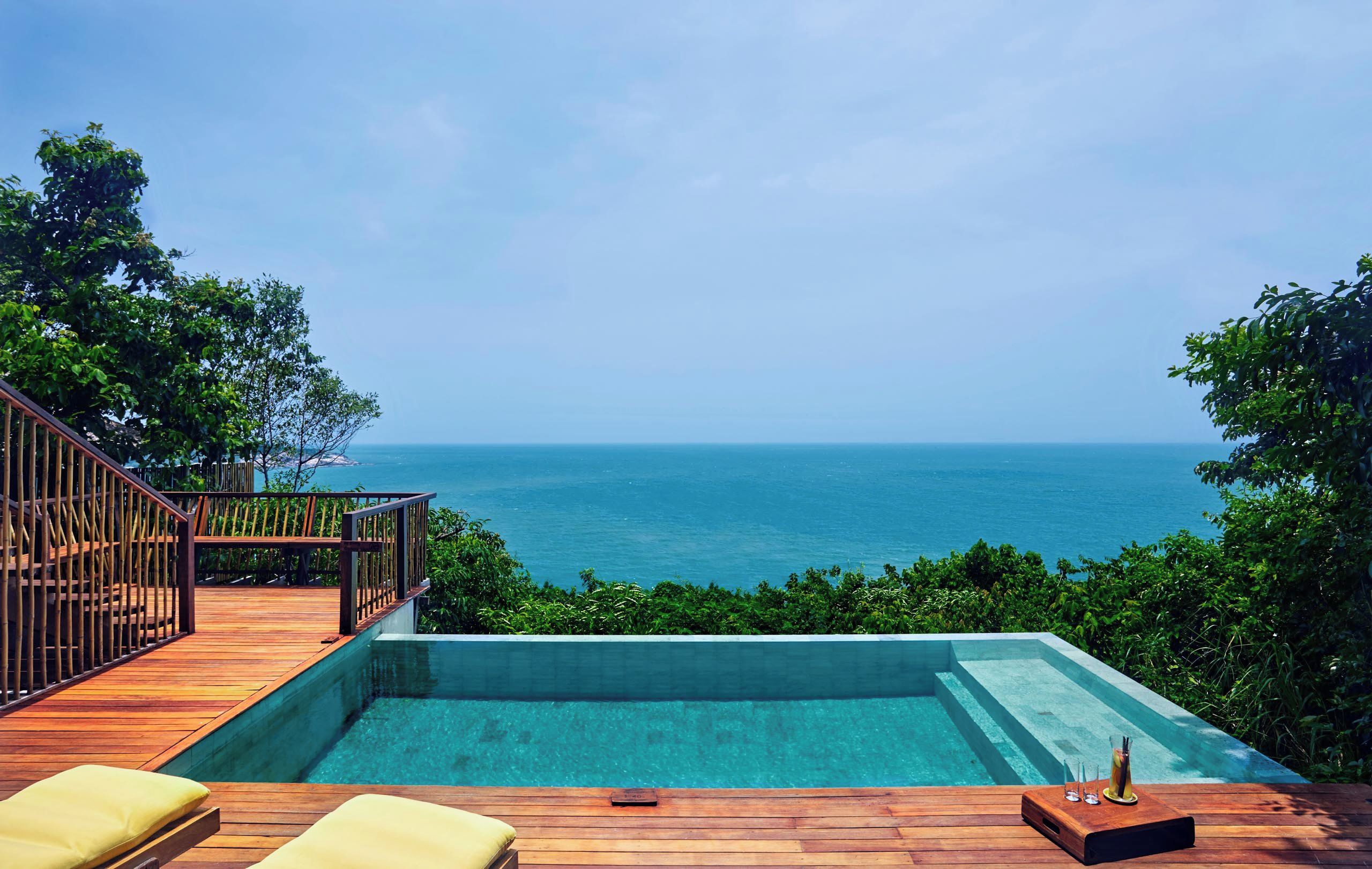 A wooden deck with a pool and lounge chairs overlooking a body of water.