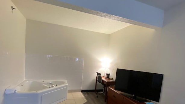 A modern living room with a large white bathtub, a wooden entertainment center, and a flat-screen TV. - Super 8 by Wyndham Ida Grove (Ida Grove)