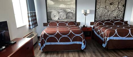 A hotel room with two beds, a TV, a desk, and a large window with curtains.