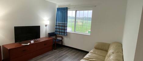 Una sala de estar con un sofá, un televisor, un mueble de madera y una ventana con cortinas.