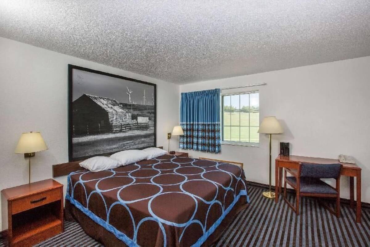 Ein Hotelzimmer mit einem großen Bett, zwei Nachttischen mit Lampen, einem Schreibtisch mit Stuhl und einem großen Fenster mit Vorhängen.
