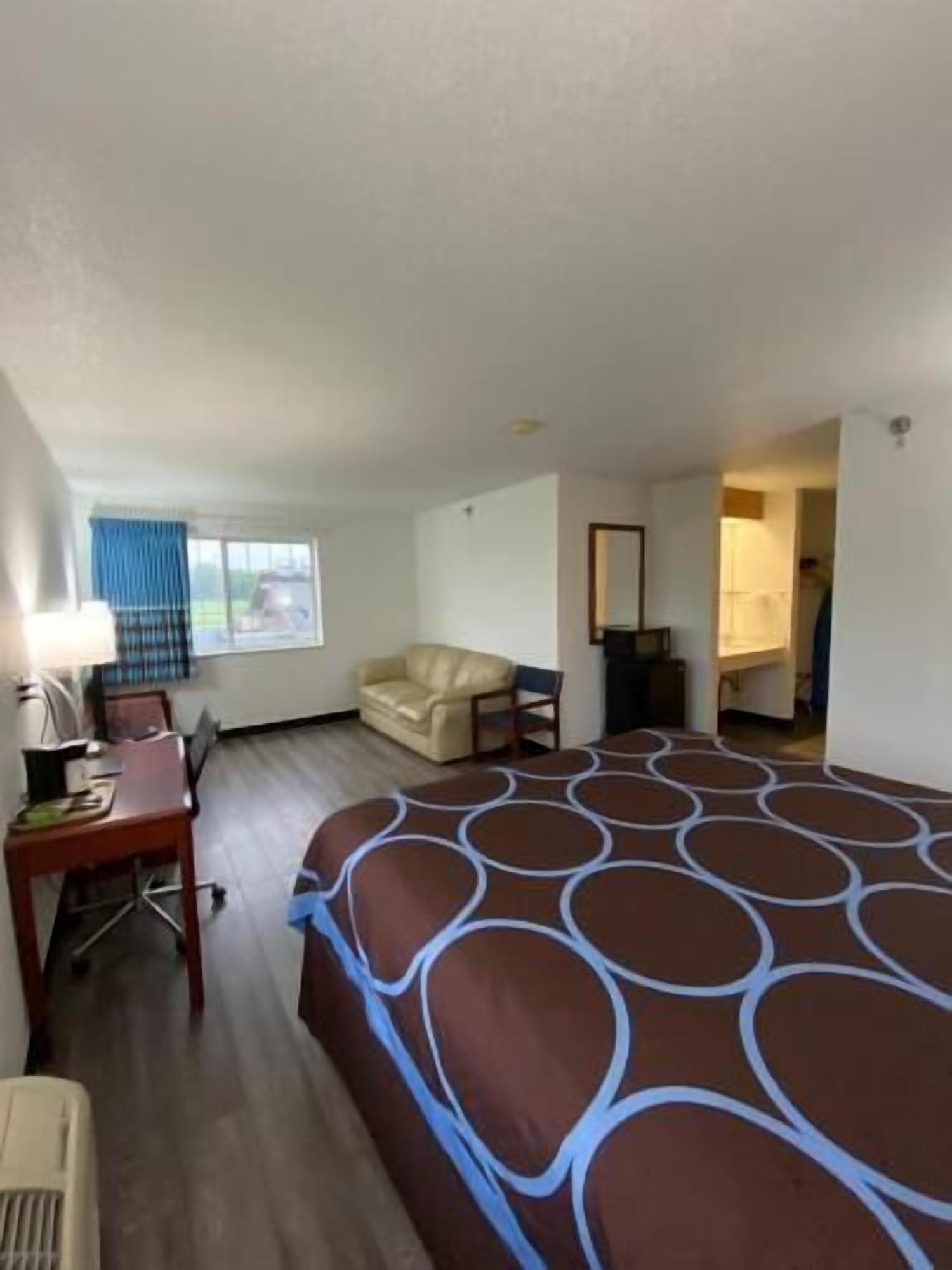 A hotel room with a bed, a desk, a chair, a sofa, a window with curtains, and a bathroom.