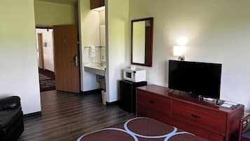 A hotel room with a wooden dresser, a flat-screen TV, a microwave, and a small desk.