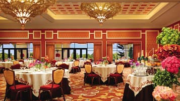 Un salón de banquetes con mesas redondas, sillas rojas y candelabros ornamentados.