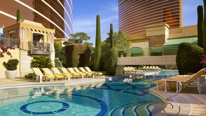 A pool area with lounge chairs and a large building in the background. - Wynn Las Vegas (Las Vegas)