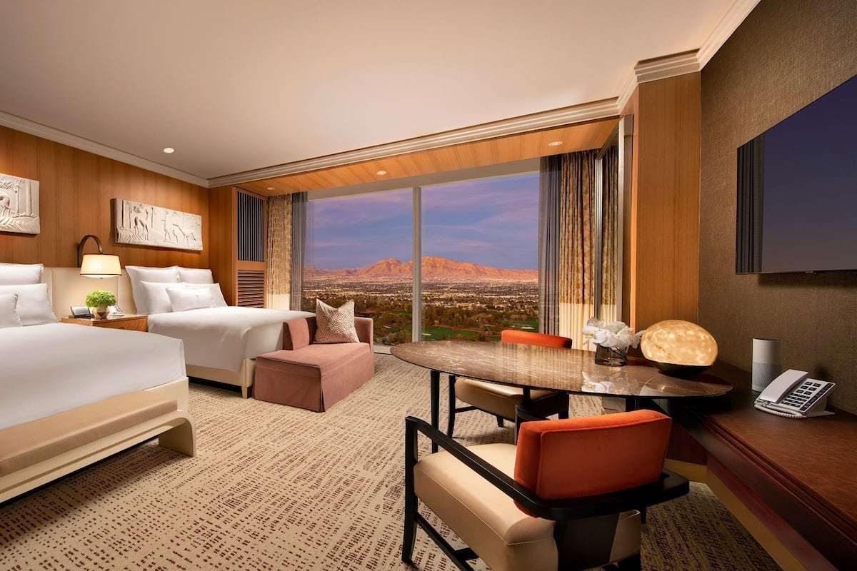A hotel room with two beds, a dining table, a sofa, and a large window with a desert view.