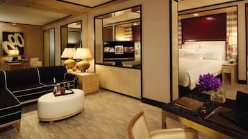 Een hotelkamer met een bed, een bureau met een laptop, een televisie, een bank en een eettafel met een bloevas.