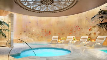 A serene indoor pool area with a decorative ceiling, lounge chairs, and a clear view of the pool.