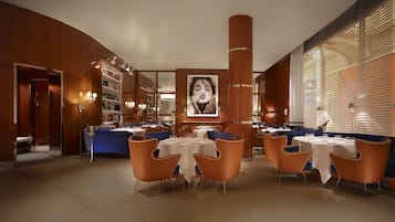 Un restaurante con mesas redondas, sillas anaranjadas y un cuadro grande en la pared.