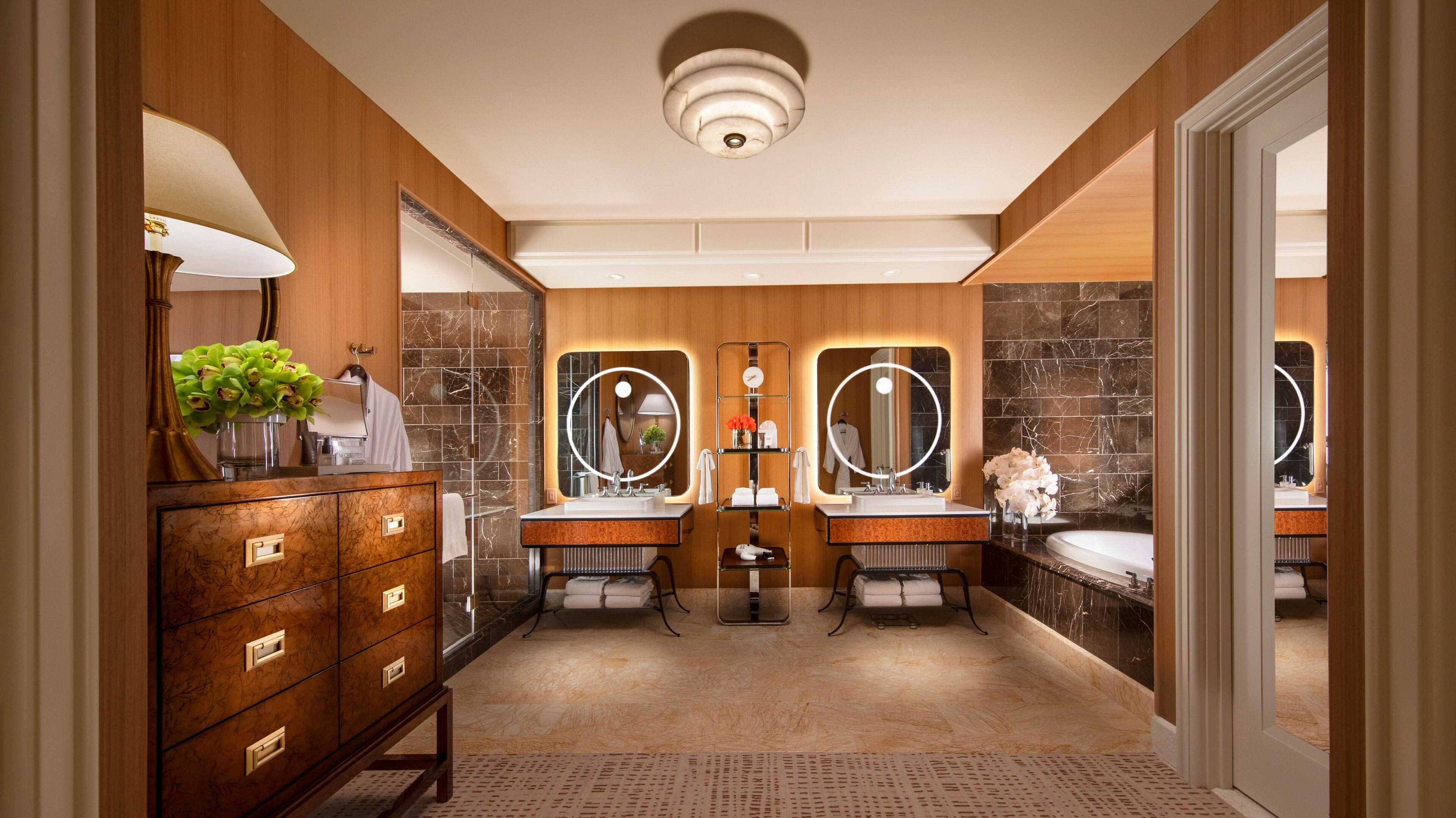 A modern bathroom with two sinks, a vanity with drawers, a mirror with a round frame, and a shower area.