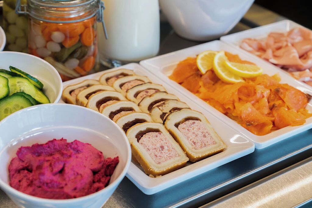 A buffet with sliced meats, pickled vegetables, and a bowl of pink dip.
