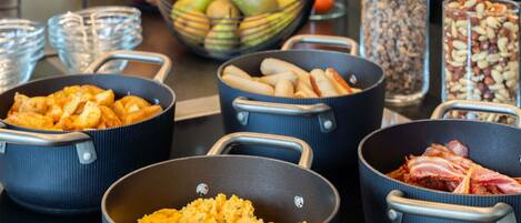A kitchen counter with various cooking pots and pans, a bowl of fruits, and jars of nuts.