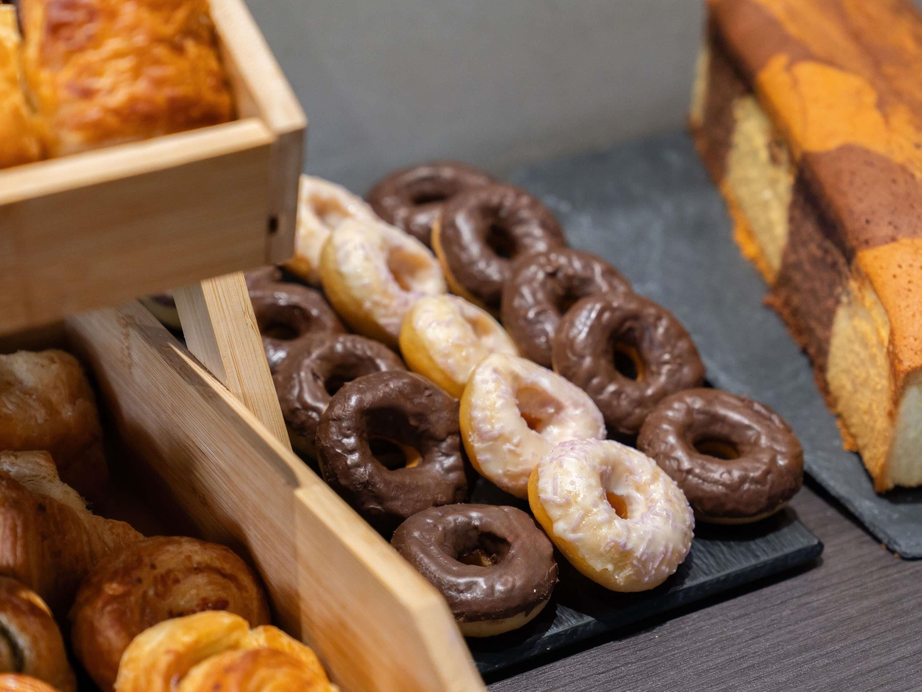 A variety of donuts and pastries in wooden and black trays.