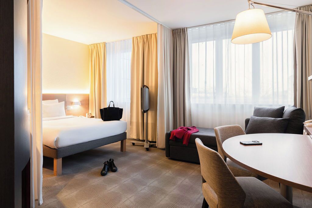 A hotel room with a bed, a sofa, a dining table, and a TV.