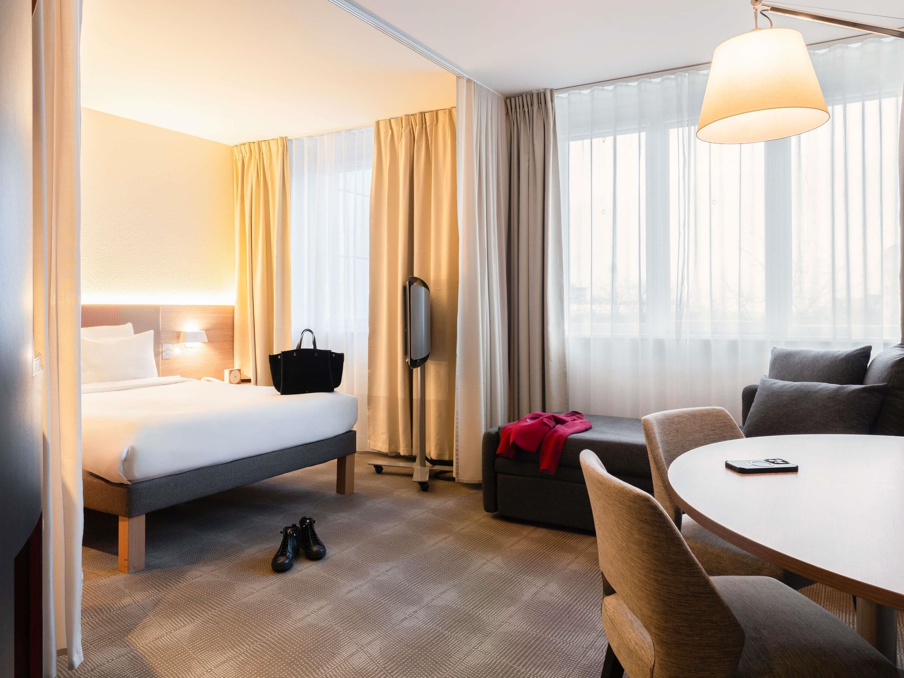 A hotel room with a bed, a desk, a chair, a television, and a window with curtains.