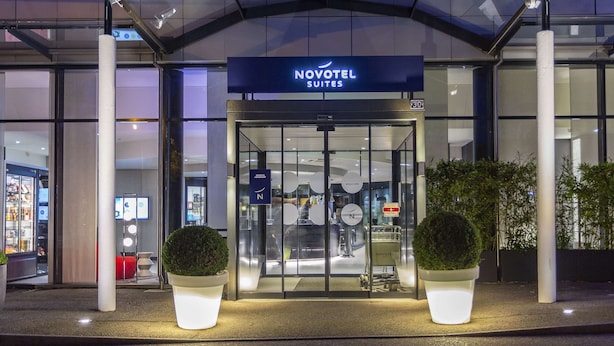 La entrada a Novotel Suites, con puerta de cristal, plantas en macetas y un cartel sobre la puerta.