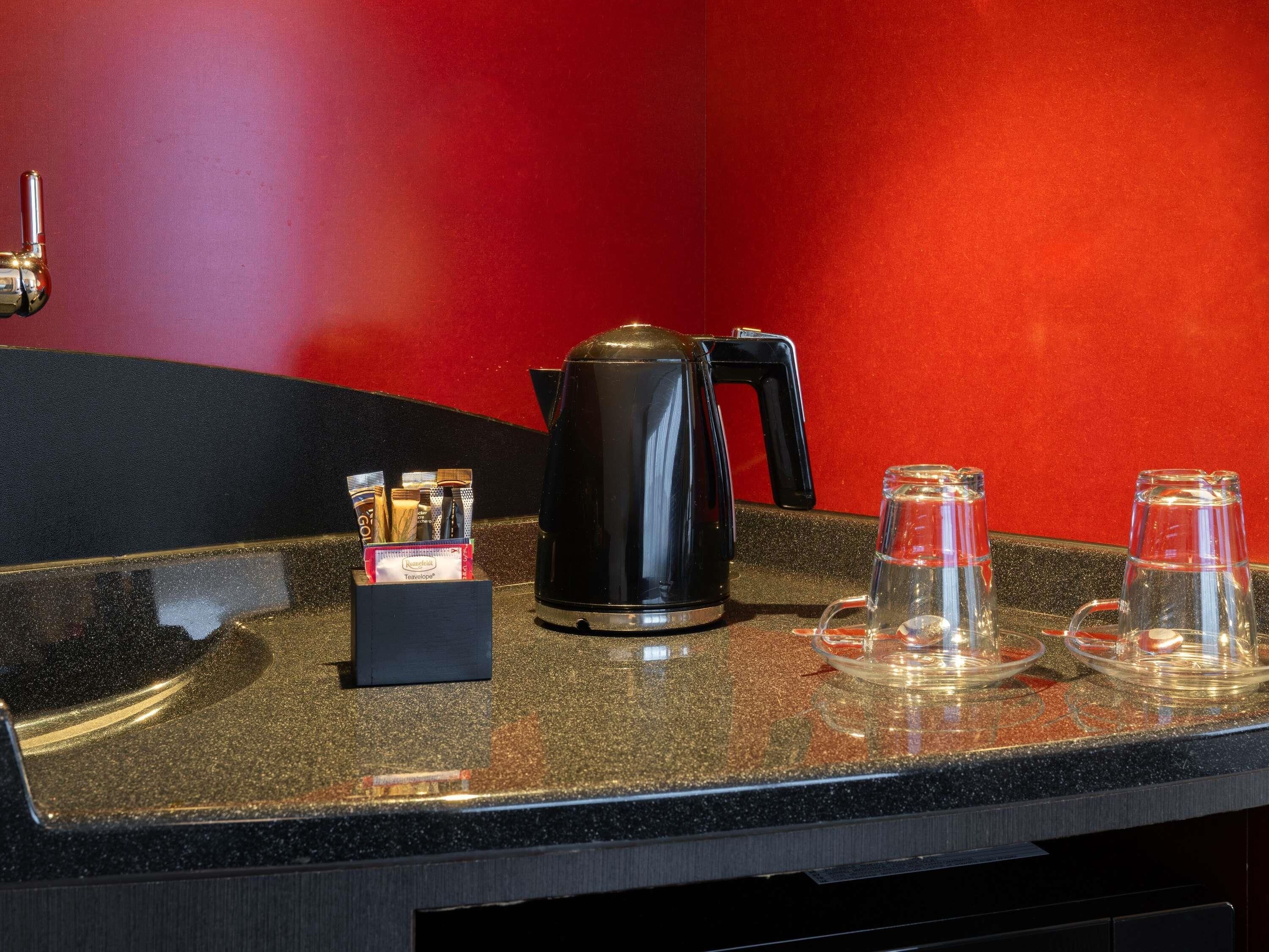 A countertop with a coffee maker, a box of tea bags, and two glass carafes on a speckled surface.
