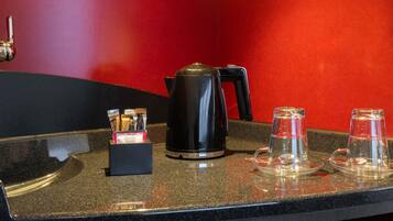 A countertop with a coffee maker, a box of tea bags, and two glass carafes on a speckled surface.