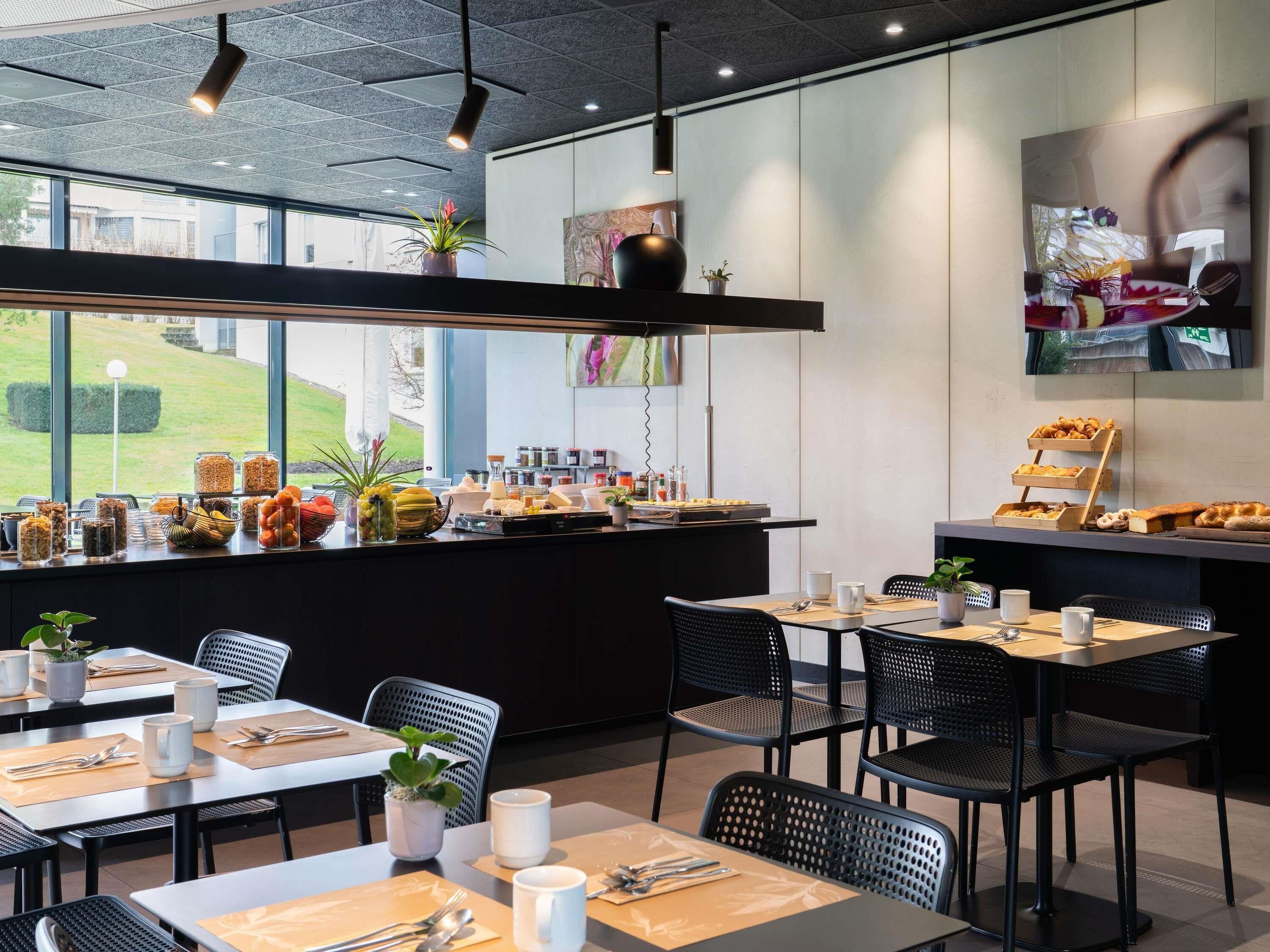 A modern cafe with tables and chairs, a counter with food and drinks, and a view of the outdoors.