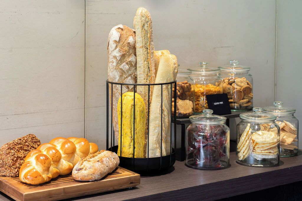 Een presentatie van diverse broden en gebak, waaronder stokbroden, croissants en koekjes, gerangschikt op een houten plank en in glazen potten.